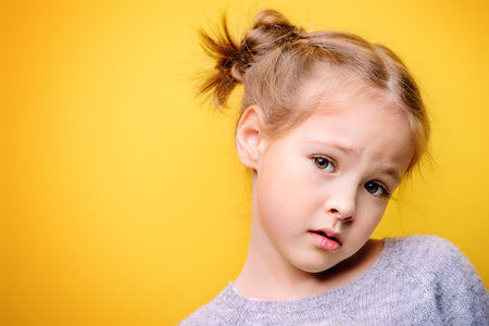 Close-up portrait of a cute little girl. Studio shot over yellow background. Childhood concept.の写真素材