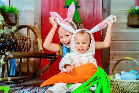 Easter holidays. Happy sister and little brother posing on the porch of a wooden house in rabbit...
