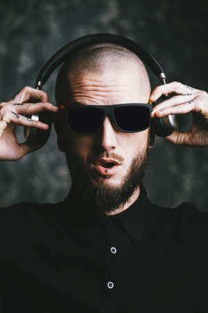 Brutal bearded man wearing sunglasses listenig to music in headphones and smiling.の写真素材