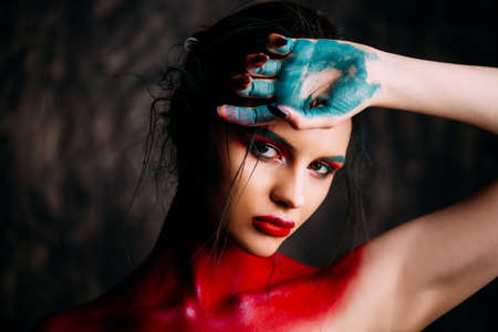 Fashion and make-up concept. Close-up portrait of an attractive young woman with creative makeup and body painting. Dark background.の写真素材