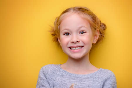 Close-up portrait of a cheerful little girl. Studio shot over yellow background. Childhood concept.の写真素材