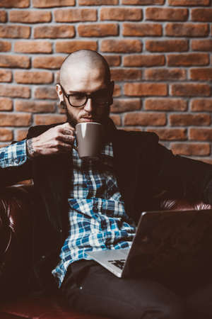 Young brutal businessman is working at home using his laptop. Male beauty, fashion. Business concept. Modern technologies.の写真素材