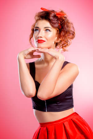 Beautiful emotional young woman wearing skirt and top blouse poses over pink background. Pin-up style. Fashion studio shot. Beauty, cosmetics.の写真素材