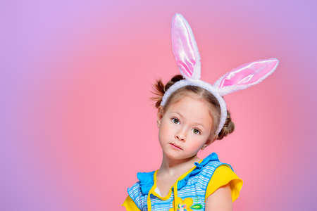 Easter holiday. Portrait of a happy little girl wearing bunny ears over pink background.の写真素材
