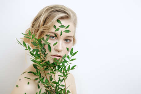 Beautiful young woman with green leaves on her face over white background. Cosmetics and makeup.の写真素材