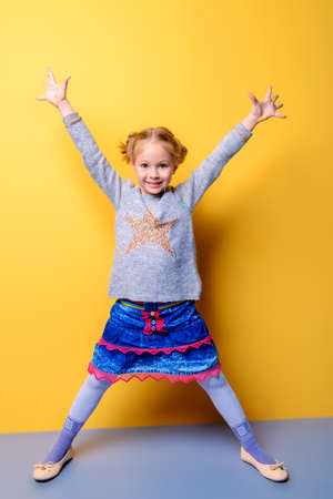 Kid's fashion. Portrait of a cute six year old girl wearing knitted clothes posing over bright yellow background. Spring, winter fashion. Happy child girl.の写真素材