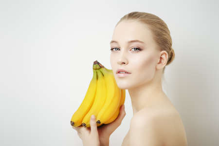 Beauty, natural cosmetics concept. Beautiful young woman with healthy shiny skin holding bananas. White background. の写真素材