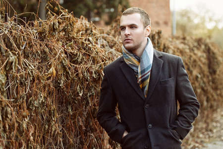 Seasonal autumn fashion. Portrait of a handsome man wearing black coat, and a scarf.  Autumn nature.の写真素材