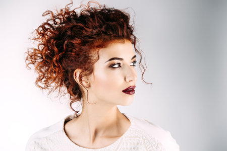 Portrait of the attractive young woman with bright red curly hair and make-up. Beauty, fashion....