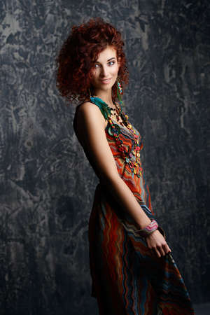 Beautiful bright woman with curly foxy hair wears a dress and beads in boho style. Ethnic style in clothes.の写真素材