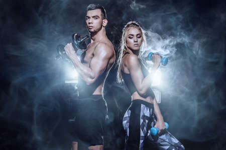 Couple of muscular young people doing exercises with dumbbells. Fitness, bodybuilding. Active, healthy lifestyle.の写真素材