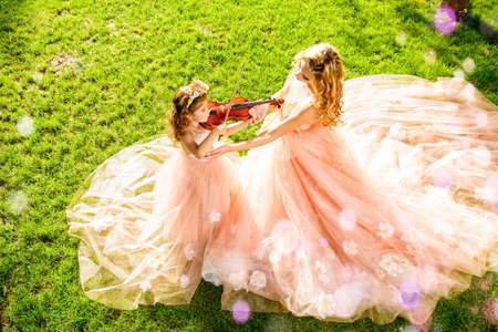 Classical music. Beautiful fairy girl teaches to play the violin a little girl. Musical fairy tales.の写真素材