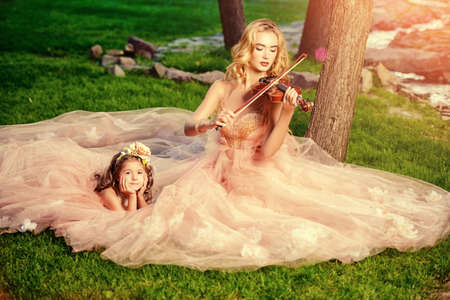 Classical music. Beautiful fairy girl teaches to play the violin a little girl. Musical fairy tales.の写真素材