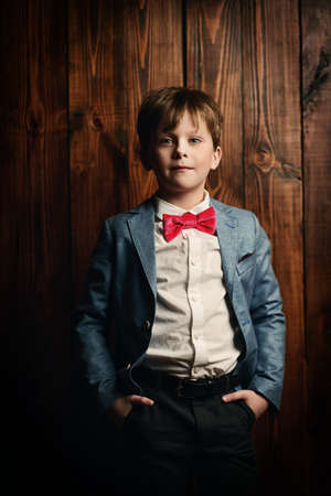Kid's fashion. Happy child boy posing at studio in elegant clothes over wooden background. Clothes for children. の写真素材
