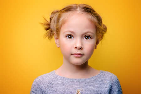 Close-up portrait of a cute little girl. Studio shot over yellow background. Childhood concept.の写真素材