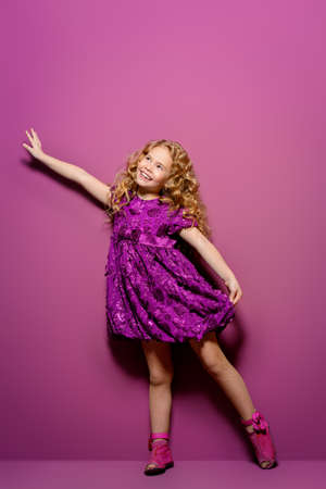 Cute little girl in a beautiful summer dress posing at studio over purple background. Kid's fashion.の写真素材