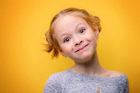 Close-up portrait of a cute little girl. Studio shot over yellow background. Childhood concept.の写真素材