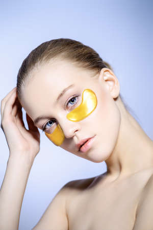 Young beautiful woman with collagen pads under her eyes on a light background. Spa, eye skin care.の写真素材