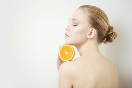Beauty, natural cosmetics concept. Beautiful young woman with healthy shiny skin holding an orange. White background. の写真素材