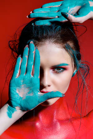 Fashion and make-up concept. Close-up portrait of an attractive young woman with creative makeup and body painting. Red background.の写真素材