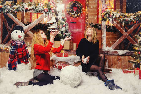 Happy girls in beautiful winter clothes make snowballs near the house, decorated for Christmas. Time of miracles. Merry Christmas and a Happy New Year.の写真素材