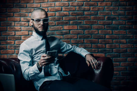 Young brutal businessman is working at home using his smartphone. Male beauty, fashion. Business concept. Modern technologies.の写真素材