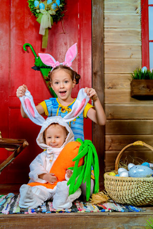 Easter holidays. Happy sister and little brother posing on the porch of a wooden house in rabbit costumes.の写真素材