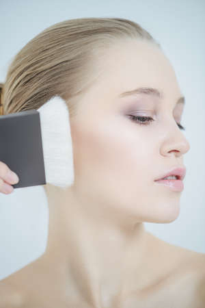 Close-up portrait of a beautiful young woman applying makeup brush. Beauty, cosmetics makeup.の写真素材
