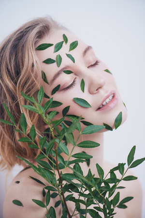 Beautiful young woman with green leaves on her face over white background. Cosmetics and makeup.の写真素材