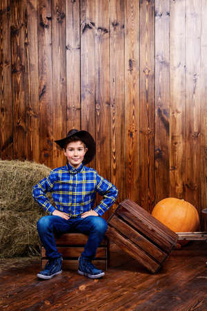 Portrait of a cute nine year old boy posing near the hay on the background of wooden wall. Western style, cowboy. Kid's fashion. Clothes for children.の写真素材