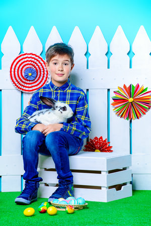 Happy child boy with Easter Bunny and painted eggs in spring decorations. Kid's fashion. Easter...