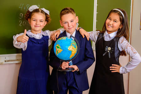 Educational concept. Three happy students standing together with a globe by a schoolboard.の写真素材