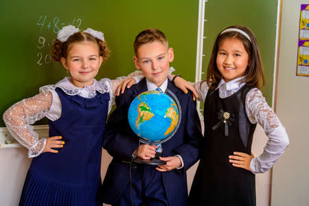 Educational concept. Three happy students standing together with a globe by a schoolboard.の写真素材
