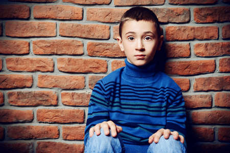 Portrait of a sad nine year old boy sit against the brick wall. Clothes for children. Kid's fashion.の写真素材