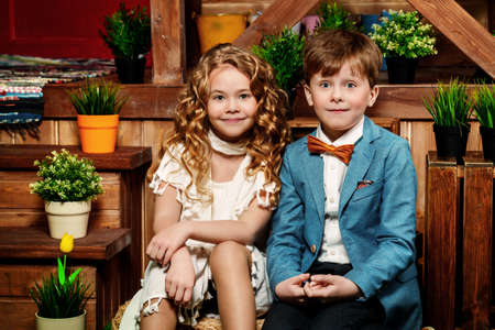 Two cute children in elegant clothes are sitting together on the porch of the house. Children's fashion. の写真素材