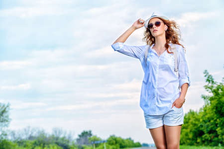 Hitchhiking girl. Attractive young woman standing on a highway and catching a passing car. の写真素材