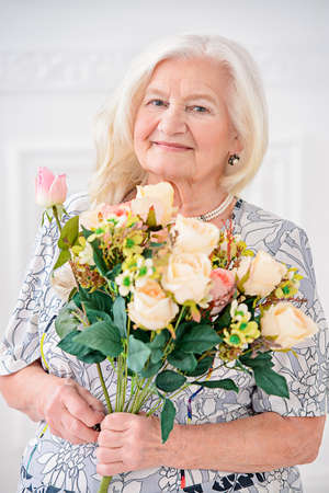 Beautiful senior woman at home with a bouquet of flowers. Happy Mother's Day. Beauty, fashion. Happy retirement. の写真素材