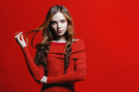 Fashion shot. Beautiful female model with long curly hair posing at studio in red dress. Red...