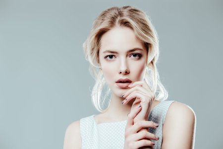 Beautiful young woman with hairstyle and make-up posing in elegant blue dress. Studio shot over blue...