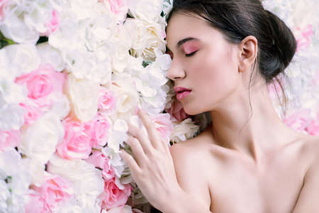 Beautiful brunette young woman with natural makeup and healthy shiny skin posing on a background of roses. Perfume, cosmetics concept.の写真素材