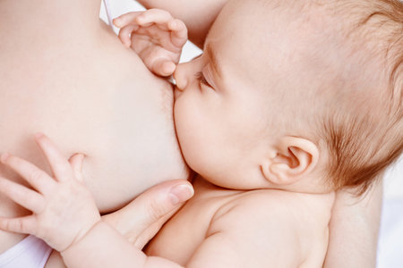 Close-up portrait of a newborn baby sucking a mother's breast. Natural feeding for babies. Baby...