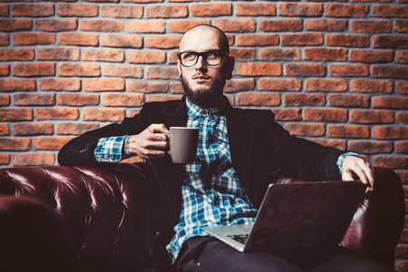 Young brutal businessman is working at home using his laptop. Male beauty, fashion. Business...