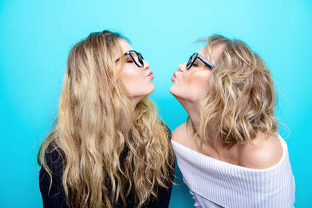 Two pretty cheerful girls in glasses are posing in studio over blue background. Beauty, fashion. Optics, eyewear.の写真素材