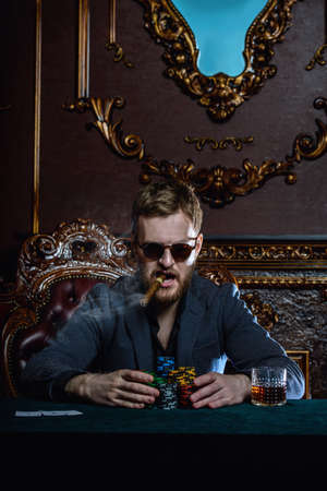 A wealthy mature man smoking cigar and playing poker in a casino. Gambling, playing cards and roulette.の写真素材
