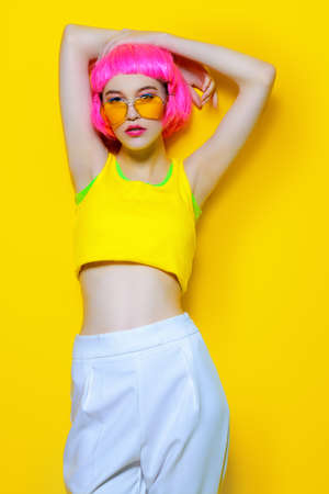 Full length portrait of a trendy girl with pink hair wearing in yellow T-shirt and white pants. Yellow background. Beauty, fashion, youth style.の写真素材