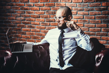 Young brutal businessman in suit working on a laptop and talking on his cell phone. Business...