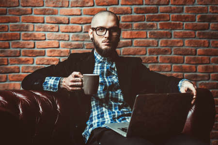 Young brutal businessman is working at home using his laptop. Male beauty, fashion. Business concept. Modern technologies.の写真素材