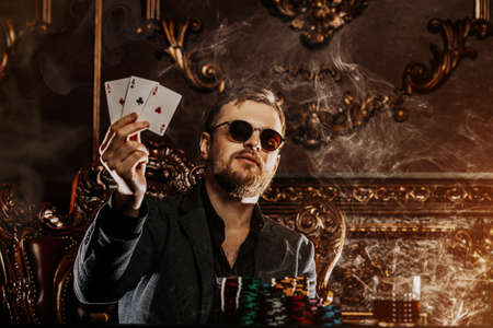 A wealthy mature man smoking cigar and playing poker in a casino. Gambling, playing cards and roulette.の写真素材