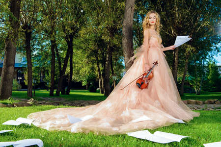 Beautiful fairy girl with the violin and sheets music on a sunny glade in the park. Musical concept. Classical music, violin.の写真素材