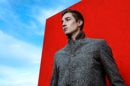 Vogue shot. Handsome fashionable man model posing outdoor over red background and a sky. 